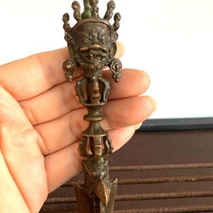 Può includere: Pugnale rituale color bronzo con dettagli intricati. L'impugnatura presenta un volto dettagliato con corona e serpente. La lama è a forma di punta di freccia. Un'opera d'arte religiosa unica.