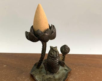 May include: A bronze incense holder featuring a lotus flower design with a cone-shaped incense stick. The holder includes an owl and a small plant. The incense holder is a decorative item.