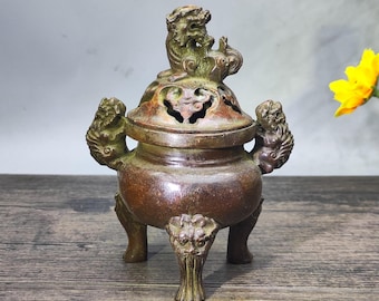 May include: A bronze incense burner with a detailed lion-like figure on the lid. The burner has three legs and handles with animal-like carvings. The lid features decorative cutouts. The overall design is ornate and antique-inspired.