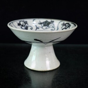 May include: A white ceramic pedestal bowl with a flared rim and a rounded base. The interior of the bowl features a blue floral pattern. The bowl is likely used for serving or display.