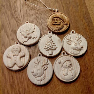 May include: A selection of wooden Christmas decorations featuring carved festive designs. The ornaments depict Santa Claus, a Christmas tree, a reindeer, a snowman, a gingerbread man, and holly. Each circular ornament has a small hole for hanging, ready for the festive season.