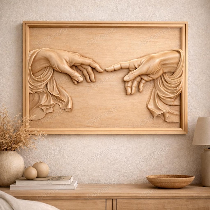 Peut inclure: Une œuvre d'art murale en bois représentant un bas-relief sculpté de deux mains presque en contact, une représentation de 'La Création d'Adam' de Michel-Ange. L'œuvre est encadrée dans un cadre en bois brun clair.