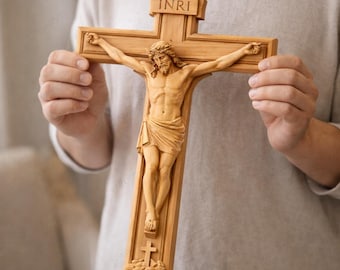 Puede incluir: Un crucifijo de madera con una talla detallada de Jesucristo. La cruz es de color marrón claro con las letras INRI en la parte superior. La figura de Jesús está esculpida con detalles intrincados, incluyendo un taparrabos drapeado.