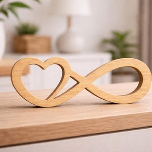 Può includere: Un simbolo dell'infinito in legno con un cuore incorporato nel design. L'intaglio in legno di colore chiaro è posto su una superficie di legno, suggerendo un oggetto decorativo o un simbolo di amore ed eternità. Lo sfondo è sfocato.