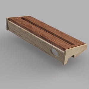 May include: A rectangular wooden desk organizer with a light-colored frame and a dark brown top. The top features two parallel grooves. The organizer has a circular cutout on one side and a small, decorative foot.