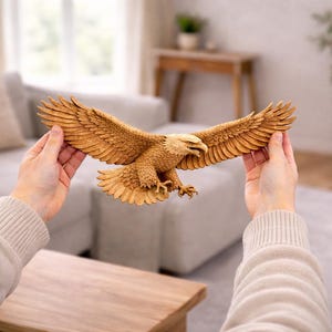 May include: A detailed wooden eagle sculpture with outstretched wings. The eagle is carved in shades of brown and beige, with intricate feather detailing. The sculpture is held in front of a blurred background, showcasing the eagle's impressive wingspan.