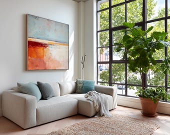 May include: A modern living room featuring a large, light-colored sectional sofa with several throw pillows in shades of blue and gray. An abstract painting with orange, red, and blue hues hangs above the sofa. A large potted plant sits near a window.