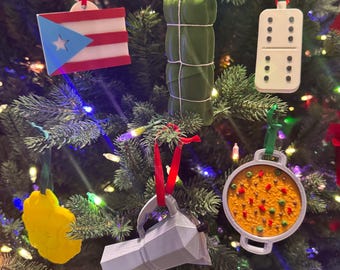 May include: Christmas tree ornaments featuring a Puerto Rican flag, a green wrapped food item, a domino, a yellow fruit, a silver coffee maker, and a paella pan. Each ornament is suspended by a red or green ribbon.