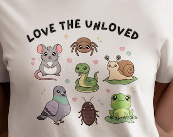 May include: A white t-shirt featuring the text LOVE THE UNLOVED in black letters above a colorful graphic illustration of a mouse, spider, snake, snail, pigeon, cockroach, and frog, all arranged in a grid pattern on the front of the garment.