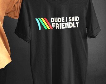 Könnte beinhalten: Schwarzes T-Shirt mit dem weißen Text "DUDE I SAID FRIENDLY". Das Shirt hat ein farbenfrohes Design aus blauem, grünem, gelbem und rotem Streifen. Das Shirt ist kurzärmlig und hat einen Rundhalsausschnitt.