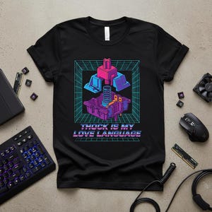 May include: Black t-shirt with a graphic design featuring a stylized mechanical keyboard switch and the text "THOCK IS MY LOVE LANGUAGE" in a retro font. The design includes pink, blue, and purple elements.