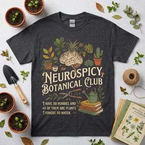 May include: Dark grey t-shirt featuring the text "NEUROSPICY BOTANICAL CLUB" and a brain illustration with plants. The shirt also says "I have 50 hobbies and 49 of them are plants, 1 forgot to water." The shirt is surrounded by gardening tools and plants.