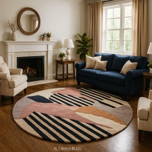May include: A circular rug with a geometric pattern in a living room. The rug has black and white stripes, and shapes in pink, beige, and navy blue. The rug is placed on a wooden floor.