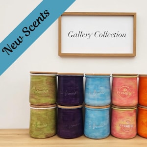 May include: Ten cylindrical ceramic jars with wooden lids arranged in two rows. The jars feature a textured, hand-painted finish in green, purple, blue, pink, and orange. Each jar displays the embossed text "La Fermi&egrave;re" and a framed sign reads "Gallery Collection" with a blue banner stating "New Scents".
