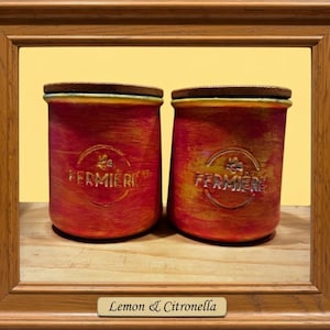 May include: Two cylindrical containers with a textured red and yellow finish, each featuring a wooden lid and the embossed text FERMIERE with a small bee icon. The containers are framed by a wooden border with a label reading Lemon & Citronella.