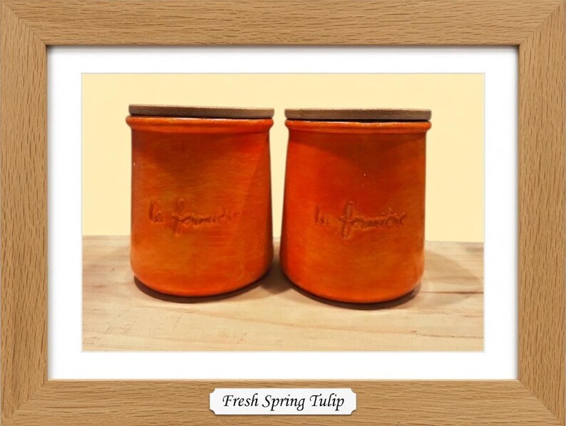 May include: Two cylindrical orange ceramic canisters with flat wooden lids. Each canister features the embossed cursive text "la fermi&egrave;re" on the front surface. The containers have a smooth, matte finish and a slightly tapered shape toward the base.