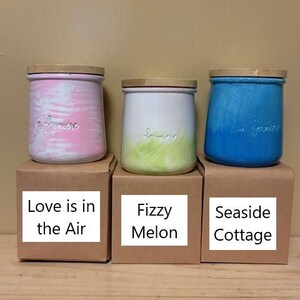 May include: Three ceramic jars with wooden lids, each featuring the embossed text la fermiere. The left jar has pink and white brushstrokes, the center jar is white with a green base, and the right jar is solid blue. Each sits on a brown box.