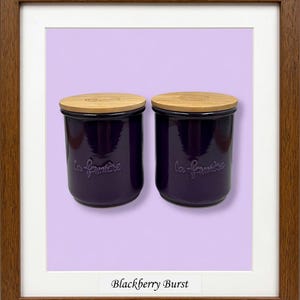 May include: Two deep purple ceramic canisters with light-colored wooden lids. Each canister features the embossed text "la fermi&egrave;re" on the front. The items are displayed within a brown wooden frame against a light purple background.