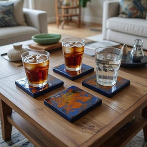 May include: Four square coasters with a blue and orange abstract design are on a wooden coffee table. Three glasses with ice and drinks are on the coasters. One glass is filled with water. The table is in a living room setting.