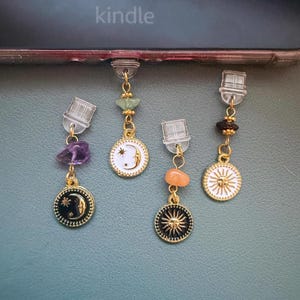 May include: Four celestial-themed earrings with gold-colored metalwork. Each earring features a different design: a moon, a sun, and gemstones. The word "kindle" is visible in the background.