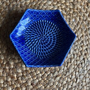 May include: A hexagonal, cobalt blue ceramic dish with a textured interior. The dish features a spiral pattern in the center and a scalloped edge design. The dish is likely used for serving or display.