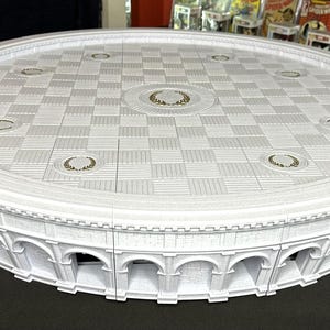 Puede incluir: Maqueta arquitectónica circular blanca con una parte superior a cuadros y una base arqueada. El modelo presenta elementos de diseño detallados, incluidos acentos decorativos y una estructura de varios niveles. El diseño general recuerda a un edificio clásico.