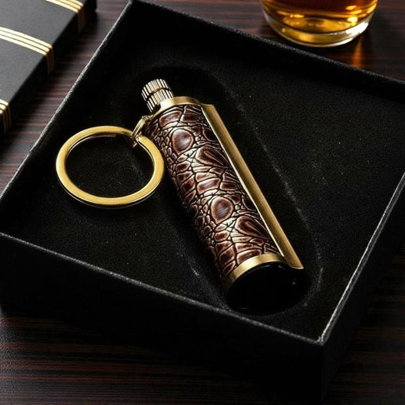 May include: A brown and gold keychain lighter with a textured, crocodile-like pattern. The lighter is in a black box, with a gold key ring attached. The lighter has a gold-coloured metal trim.