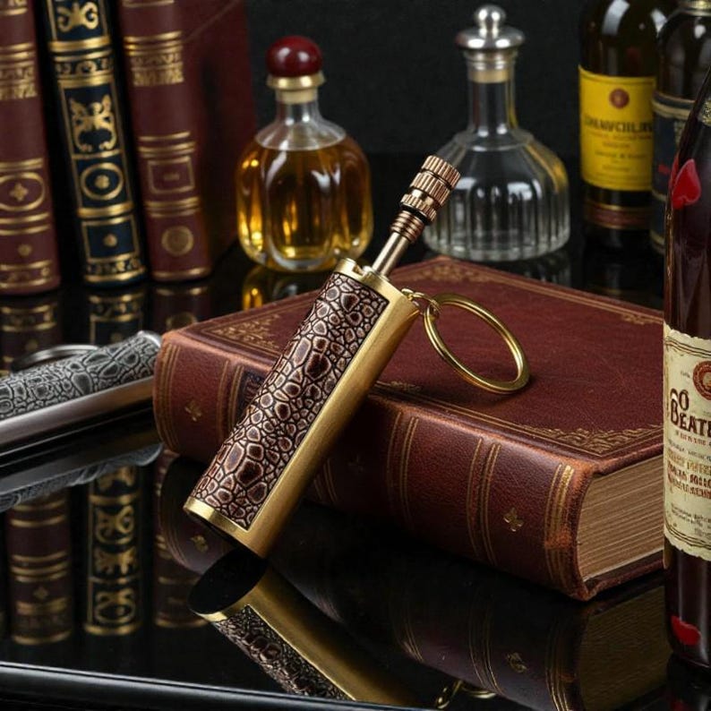 May include: A decorative brass lighter with a brown faux-leather crocodile skin pattern. The lighter has a gold keyring attached. The background includes antique books, bottles of liquor, and a knife.