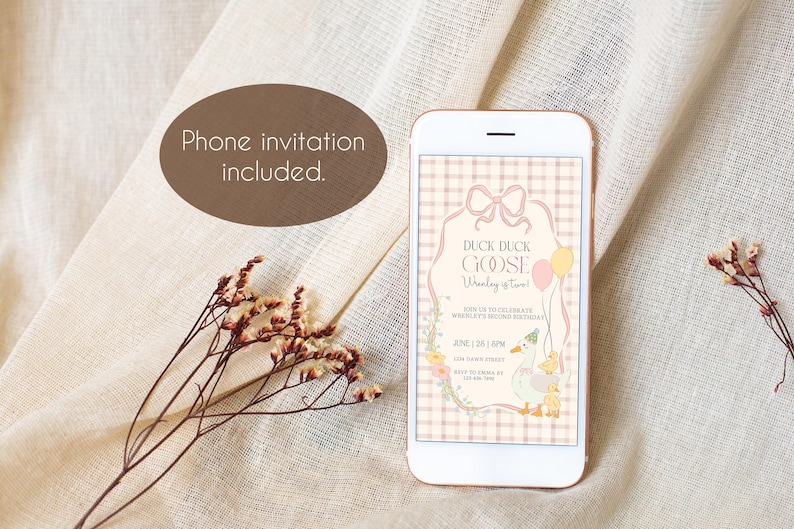 May include: A smartphone displays a digital invitation with the text "Duck Duck Goose, [Child's Name] is Two!" The invitation features a pink and beige color scheme with floral and balloon accents. A sprig of dried flowers and a brown oval with the text "Phone invitation included" are also in the image.