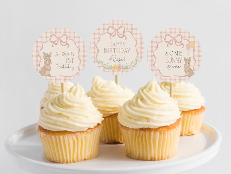 May include: Four cupcakes with pink and white checkered cupcake toppers. The toppers feature a bunny rabbit and the text "Alisa's 1st Birthday", "Happy Birthday Alisa!" and "Some Bunny is One".