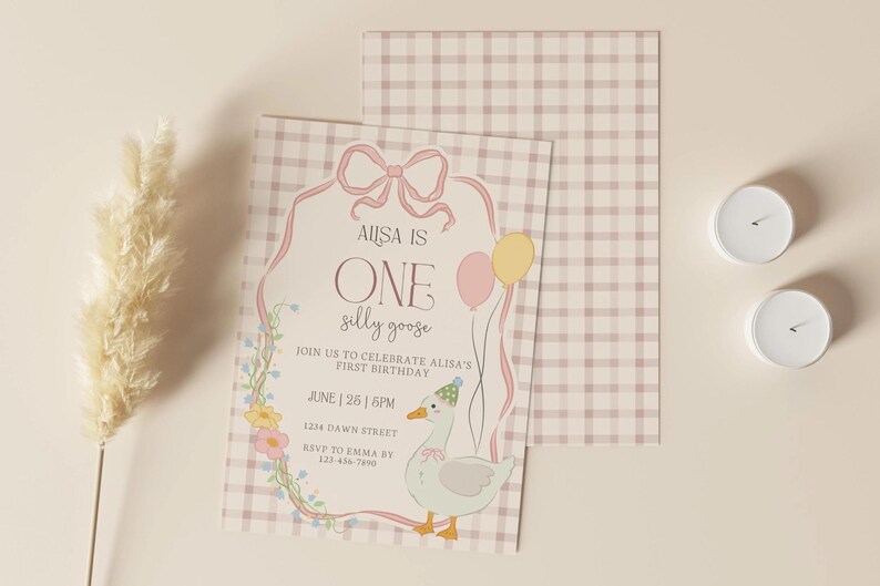 May include: A birthday invitation with a whimsical design. The invitation features a cartoon goose, balloons, and floral accents. The text reads "AUSA IS ONE silly goose" and includes event details. Two white candles and a decorative plant are also present.