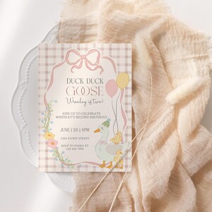 May include: A pastel-colored birthday invitation with the text "Duck Duck Goose Wrenley is two!" features a cartoon goose and ducklings. The invitation is on a white plate with a peach-colored fabric in the background.