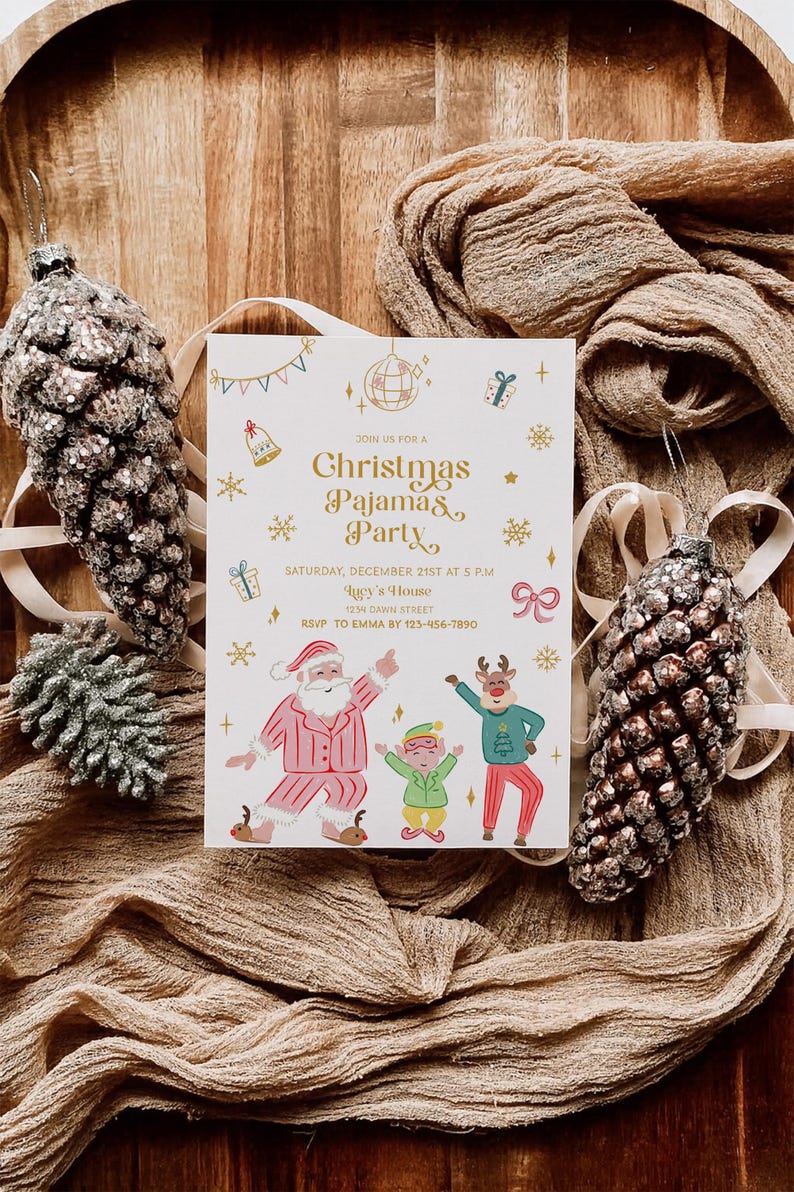 Op de afbeelding: Een uitnodigingskaart voor een kerstpyjamaparty met de kerstman, een rendier en een elf die dansen. De uitnodiging heeft gouden tekst en feestelijke illustraties op een witte achtergrond. Twee glinsterende dennenappelornamenten en beige stof omringen de kaart.