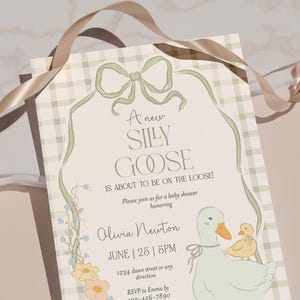 以下が含まれることがあります： 風変わりなデザインのベビーシャワーの招待状。「A new SILLY GOOSE is about to be on the loose!」というテキストが装飾的なフォントで表示され、ガチョウとガチョウの絵が描かれています。招待状は、緑のリボンと花のアクセントで飾られています。