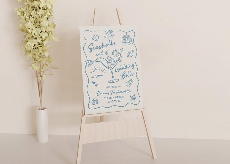 May include: A wooden easel supports a sign with blue illustrations and text. The sign says "Seashells and Wedding Bells" with a mermaid in a cocktail glass. Additional text welcomes guests to Emma's Bachelorette in Tulum, Mexico.