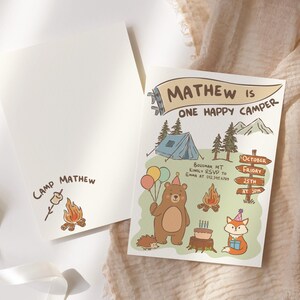 Puede incluir: Un juego de dos tarjetas de invitaci&oacute;n color crema. Una tarjeta presenta el texto "Camp Mathew" con una ilustraci&oacute;n de fogata y malvavisco. La otra tarjeta tiene una ilustraci&oacute;n con tem&aacute;tica de campamento con el texto "Mathew is One Happy Camper".