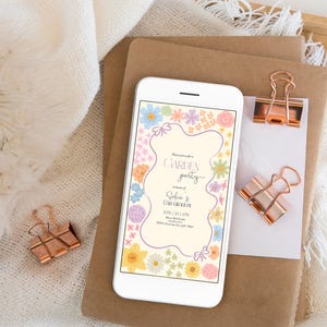 May include: A digital invitation on a smartphone screen with a floral border and the text "Garden Party" in honor of Sofia & David. The invitation includes the date, time, and location of the event.