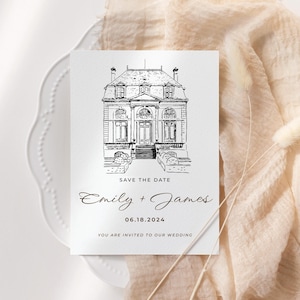 Puede incluir: Tarjeta de invitaci&oacute;n de boda blanca con un dibujo lineal negro de un edificio se&ntilde;orial. El texto "SAVE THE DATE" est&aacute; sobre los nombres "Emily + James" y la fecha "06.18.2024". La tarjeta est&aacute; sobre un plato blanco con una tela beige.