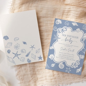 May include: Two baby shower invitations. One is white with blue seashell illustrations. The other is blue with a white frame and the text "Sea You Soon baby". The invitations are on a beige fabric.
