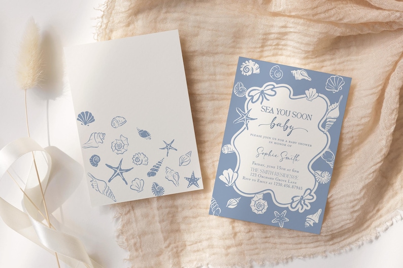 May include: Two baby shower invitations. One is white with blue seashell illustrations. The other is blue with a white frame and the text "Sea You Soon baby". The invitations are on a beige fabric.