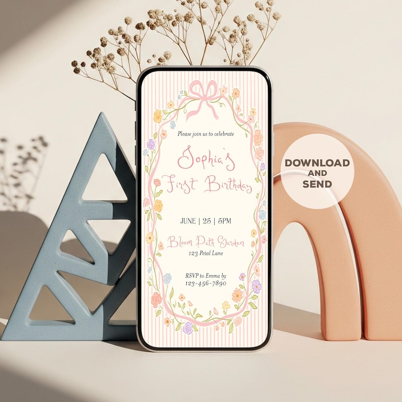 May include: A smartphone screen shows a digital invitation for Sophia's First Birthday. The invitation has a floral wreath design with the text "Sophia's First Birthday" and event details. A pink ribbon and bow are at the top. The phone is surrounded by decorative elements.