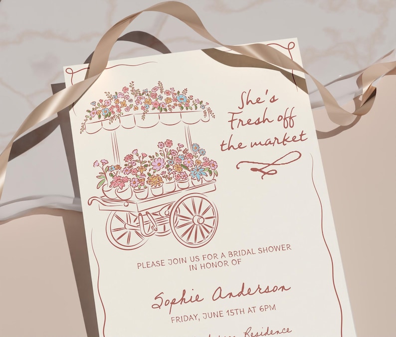 May include: Cream-colored invitation with a floral cart illustration in brown ink. Text reads "She's Fresh off the market" and details for a bridal shower. A tan ribbon is draped across the top.