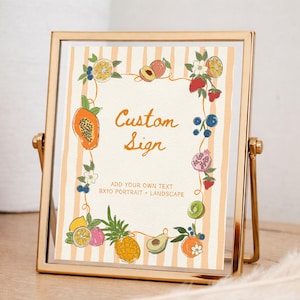 May include: A gold metal frame holds a sign with a cream background and vertical peach stripes. The sign features a border of colorful illustrated fruits and flowers, with the text "Custom Sign" and "ADD YOUR OWN TEXT 8X10 PORTRAIT + LANDSCAPE".
