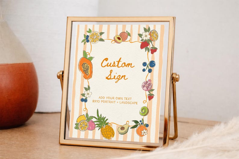 May include: A gold metal frame holds a sign with a cream background and vertical peach stripes. The sign features a border of colorful illustrated fruits and flowers, with the text "Custom Sign" and "ADD YOUR OWN TEXT 8X10 PORTRAIT + LANDSCAPE".