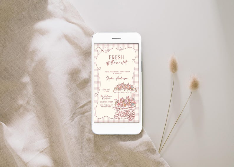 May include: A smartphone displays a floral-themed invitation with the text "Fresh off the market." The invitation features a cart filled with flowers and is set against a checkered background. Two dried flower stems are on the right.