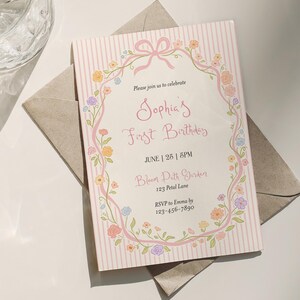 May include: A pink and white invitation card for Sophia's First Birthday, with floral and ribbon accents. The card includes the event details: June 25th, 6 PM, Bloom Path Garden, and an RSVP contact. The card is on a neutral envelope.