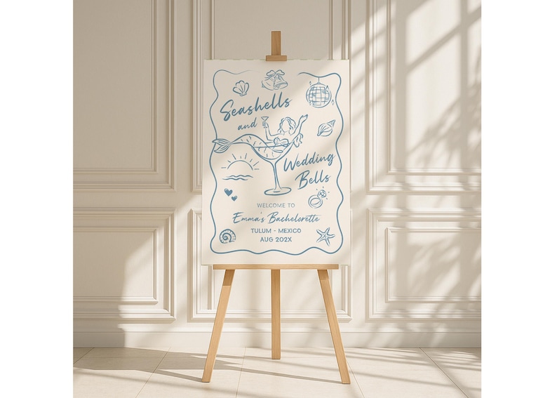 May include: A light beige welcome sign on a wooden easel. The sign features blue line art with the words "Seashells and Wedding Bells" and a mermaid in a cocktail glass. The sign welcomes guests to Emma's Bachelorette in Tulum, Mexico, August 202X.