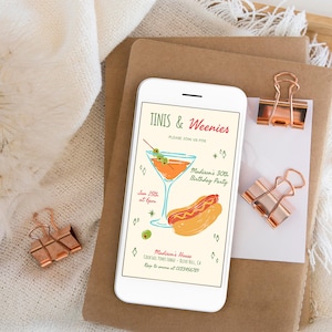 May include: A smartphone displays a party invitation with the text "Tinis & Weenies." The invitation features a cocktail and hot dog illustration. The phone rests on a stack of brown paper with copper-colored binder clips.