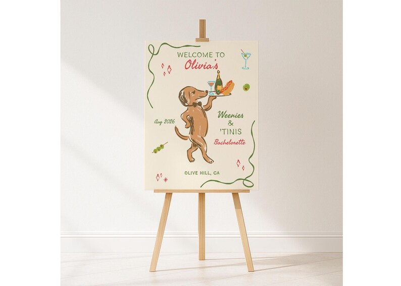 May include: A rectangular welcome sign on a wooden easel featuring a brown dachshund wearing a bowtie and carrying a tray with a bottle and hot dog. Text reads: WELCOME TO Olivia's, Weenies & 'Tinis Bachelorette, Aug 2026, and OLIVE HILL, CA.