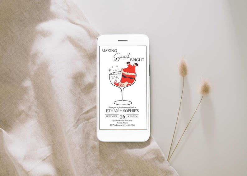 May include: A white smartphone displays a Christmas cocktail invitation. The invitation features a Santa Claus illustration inside a cocktail glass, with the text "Making Spirits Bright." The invitation includes event details.